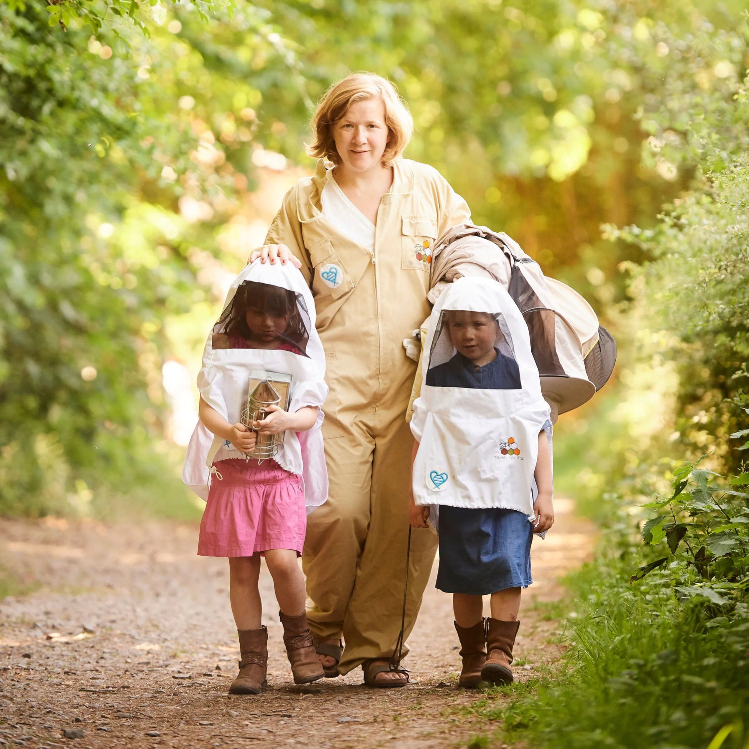 Initiation à l’apiculture avec HabeebeeCulture : une apicultrice et deux enfants en combinaison découvrent le monde des abeilles en pleine nature.
Introductie tot bijenteelt met HabeebeeCulture: een imker en twee kinderen in beschermkledij verkennen de wereld van de bijen in de natuur.
Beekeeping introduction with HabeebeeCulture: a beekeeper and two children in protective gear exploring the world of bees in nature.
