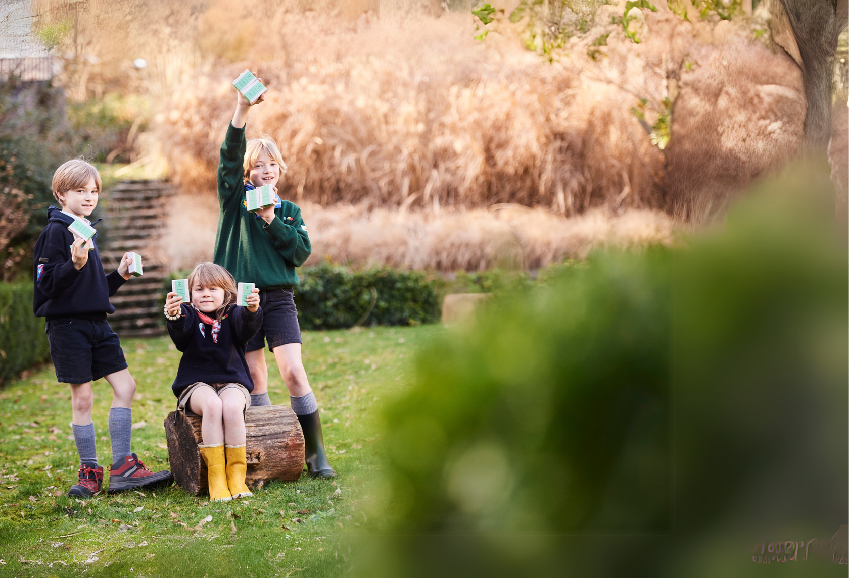 Trois enfants scouts célèbrent fièrement les savons Habeebee dans un jardin – Une image inspirante qui illustre le soutien joyeux aux bonnes initiatives locales et durables. Drie scouts vieren enthousiast de Habeebee-zepen in een tuin – Een inspirerend beeld dat blijk geeft van steun aan lokale en duurzame initiatieven. Three scout children proudly holding Habeebee soaps in a garden – An uplifting scene that supports positive, local and sustainable actions.