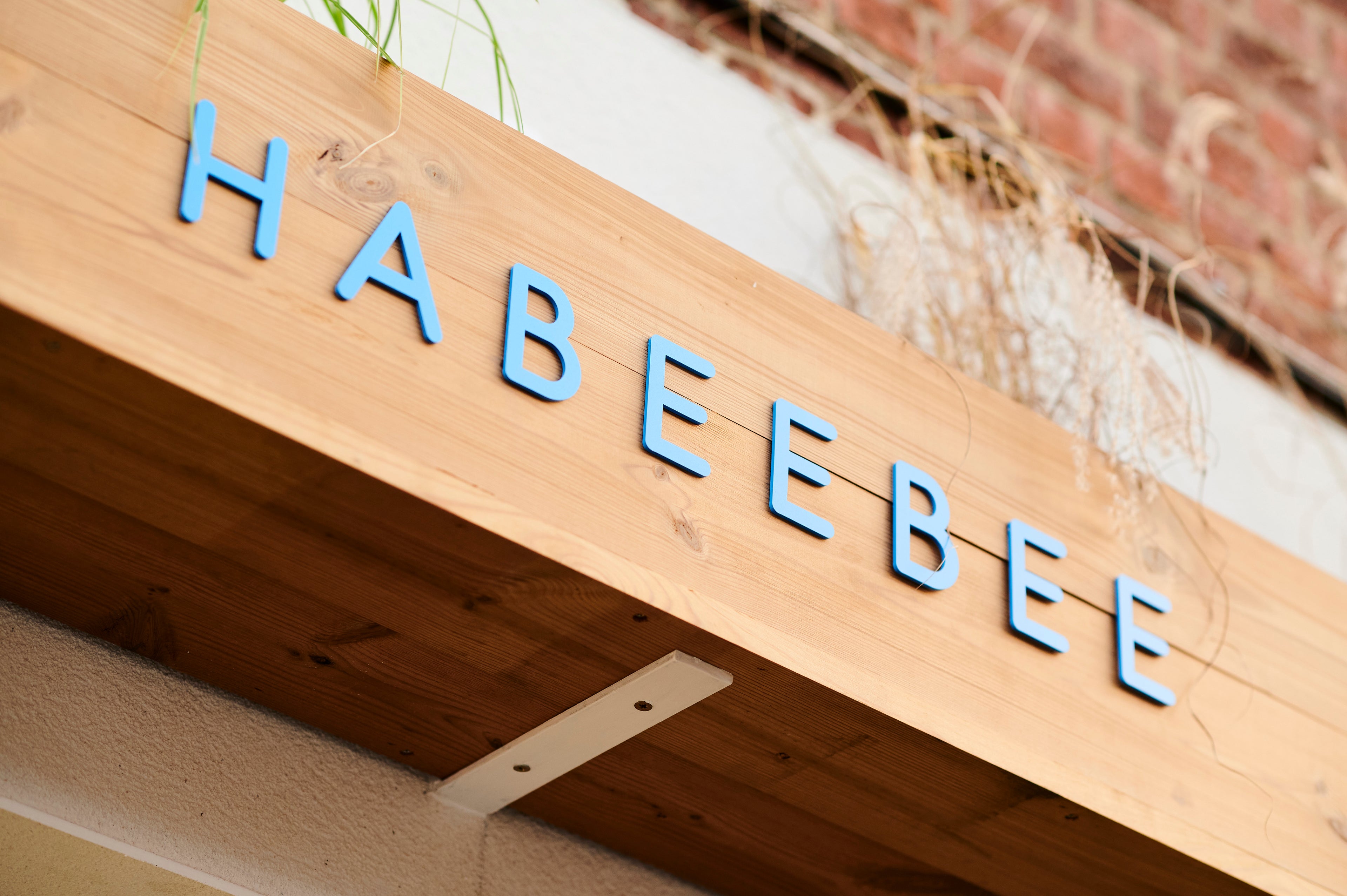 Enseigne en bois de la Savonnerie Habeebee à Bruxelles – Une invitation chaleureuse à pousser la porte de notre boutique artisanale et à entrer en contact. Houten uithangbord van de Savonnerie Habeebee in Brussel – Een warme uitnodiging om onze ambachtelijke winkel binnen te stappen en contact op te nemen. Wooden sign of the Habeebee Soap Factory in Brussels – A warm invitation to step into our artisanal shop and get in touch.